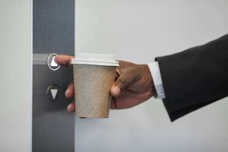 Close up of unrecognizable businessman pressing elevator button in office building and holding...