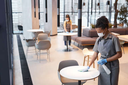 Portrait of two female workers wearing masks while cleaning tables in cafe interior, safety concept, copy spaceの写真素材