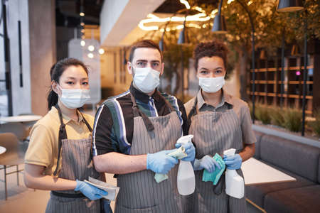 Waist up portrait of three cafe workers wearing masks and looking at cameraの写真素材