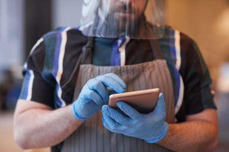 Cropped portrait of waiter wearing face shield and gloves while taking order in cafe with covid safety measures, copy spaceの写真素材