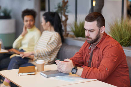Portrait of bearded man working at table in cafe and looking at smartphone screen, copy spaceの写真素材