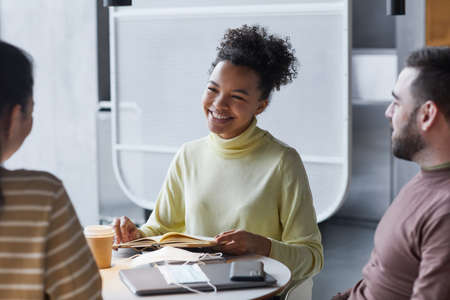 Group of multi-ethnic young people studying together at table in cafe or library, focus on African-American teenager smiling, copy spaceの写真素材