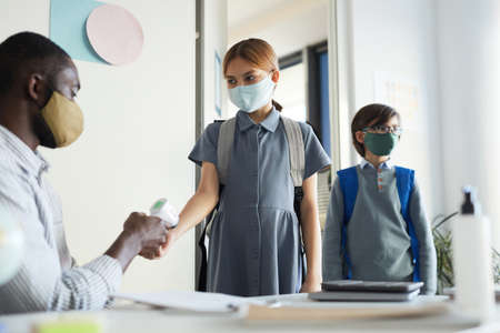 Portrait of male teacher checking temperature of children entering classroom in school, safety measuresの写真素材
