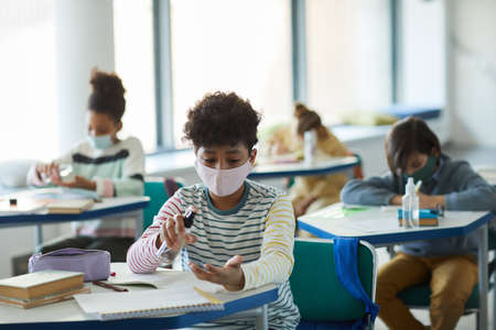 Portrait of young African-American boy sanitizing hands in school classroom, safety measures, copy spaceの写真素材