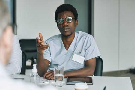 Portrait of young African-American doctor speaking to colleagues during medical meeting in conference roomの写真素材