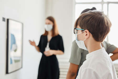 Side view at group of children looking at paintings in art gallery and wearing masks, copy spaceの写真素材