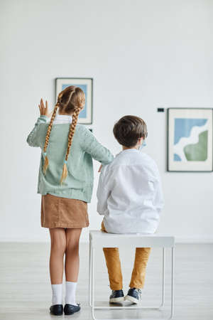 Vertical back view at boy and girl looking at paintings in art galleryの写真素材