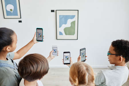 High angle view at diverse group of children holding smartphones in art gallery and taking photos of paintings, digital world, copy spaceの写真素材