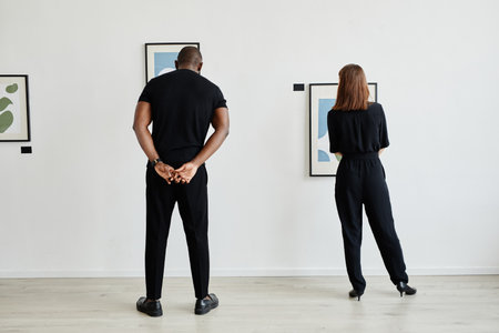 Minimal back view portrait of modern couple looking at paintings in contemporary art gallery, copy spaceの写真素材