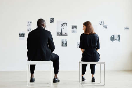 Full length back view at elegant couple looking at black and white photographs in modern art gallery, copy spaceの写真素材