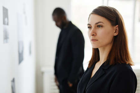 Minimal side view portrait of elegant young woman wearing black while looking at paintings in modern...