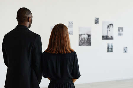 Minimal back view at two people wearing black while looking at photographs in modern art gallery, copy spaceの写真素材