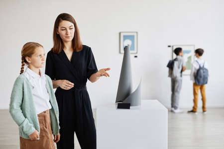 Portrait of mother and daughter looking at sculptures in modern art gallery, copy spaceの写真素材