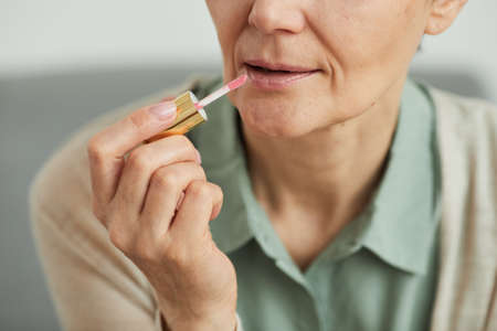 Close up of unrecognizable mature woman putting on lipstick while doing makeup at home, copy spaceの写真素材