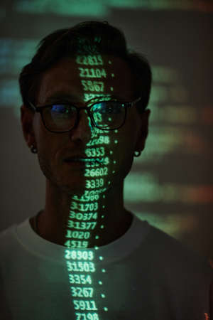 Hacker working on personal computer projecting code numbers and characters reflect on his faceの写真素材