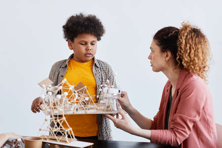 Portrait of teen boy presenting school project to female teacher during art and craft lesson in schoolの写真素材