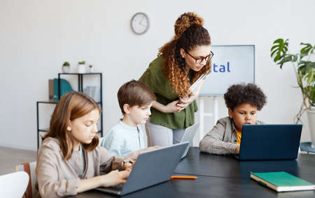 Diverse group of children using computers during IT class in school with young female teacherの写真素材