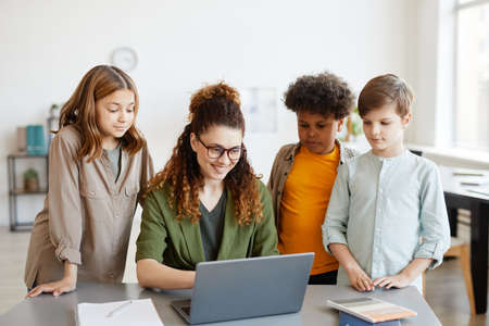 Portrait of young female teacher using computer with diverse group of childrenの写真素材