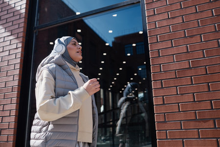 Low angle portrait of modern Middle-Eastern woman running in city lit by sunlight and wearing...