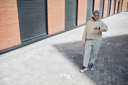 High angle angle portrait of contemporary Middle-Eastern woman checking smartwatch during morning...
