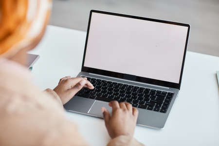 Close up of modern African-American woman using laptop in office with focus on blank white screen,...
