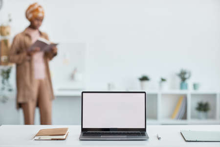 Close up of open laptop with blank white screen with ethnic women working in background, copy space