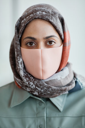 Vertical close up portrait of modern Middle-Eastern woman wearing mask and looking at camera