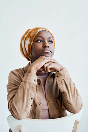 Vertical portrait of modern African-American woman looking away and wearing headscarf while posing against white wallの写真素材