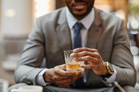 Cropped shot of successful African-American businessman enjoying glass of whiskey in hotel, copy spaceの写真素材