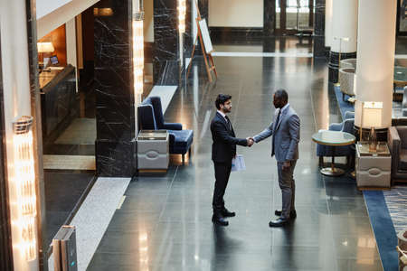 Wide angle view at two business partners shaking hands while standing in luxurious hotel lobby, copy spaceの写真素材