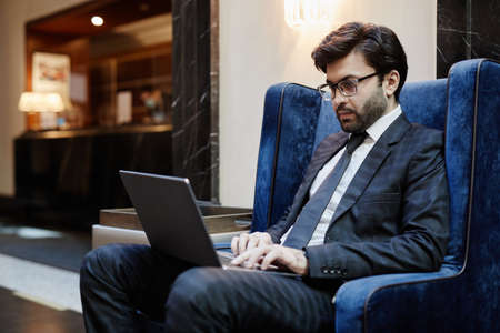 Portrait of successful Middle-Eastern businessman using laptop while working in hotel lobby on business trip, copy spaceの写真素材