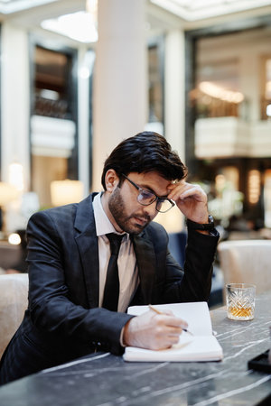 Vertical portrait of successful Middle-Eastern businessman working in hotel lobby during business...