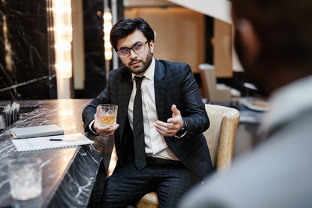 Portrait of successful Middle-Eastern businessman talking to partner at bar in hotel during business...