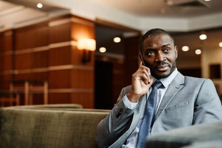 Portrait of African-American businessman speaking by smartphone at hotel lobby during business trip, copy spaceの写真素材
