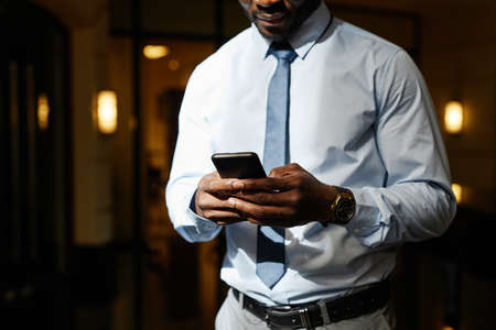 Cropped shot of unrecognizable African-American businessman using smartphone in sunlight, copy spaceの写真素材