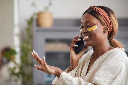 Side view portrait of young African-American woman enjoying beauty routine at home and speaking by...