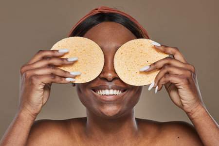 Portrait of playful African-American woman enjoying skincare and holding natural spongesの写真素材
