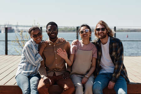 Diverse group of young people smiling at camera while posing outdoors by river, all wearing sunglassesの写真素材