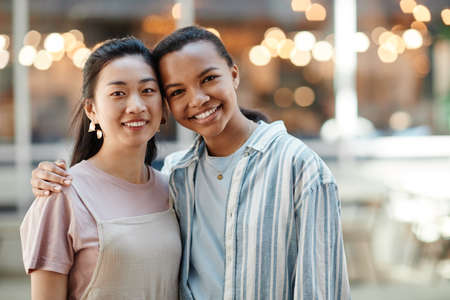 Waist up portrait of two ethnic young women looking at camera while posing outdoors in city, copy spaceの写真素材