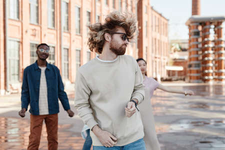 Diverse group of contemporary young people dancing outdoors in city street, focus on carefree man in foregroundの写真素材