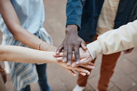 Close up of multi-ethnic group of young people stacking hands outdoors and celebrating friendship,...