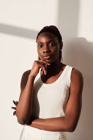 Vertical portrait of sportive African-American woman looking at camera while posing against white in...