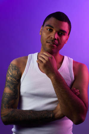 Vertical portrait of tattooed mixed-race man looking at camera while posing against purple background in studio, copy spaceの写真素材