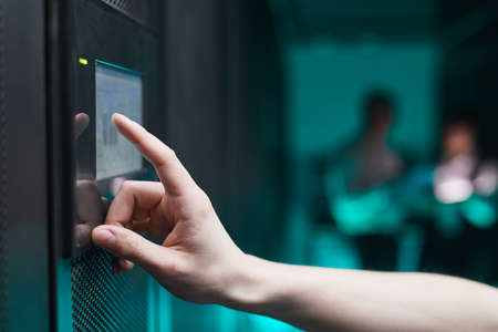 Side view close up of unrecognizable man operating server cabinet via digital control panel in data...