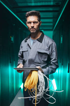 Vertical portrait of mature network engineer using digital tablet in server room during maintenance...