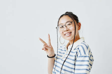 Minimal portrait of Asian teenage girl posing and looking at camera against white background, copy...