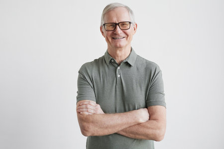 Minimal waist up portrait of smiling senior man looking at camera while standing with arms crossed...