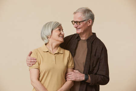 Minimal waist up portrait of carefree senior couple embracing and looking at each other while...