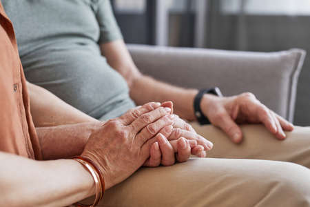 Close up of loving senior couple holding hands while sitting on couch together, copy space