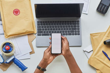 Top down view at female hands holding smartphone with blank screen over workplace at shipping...